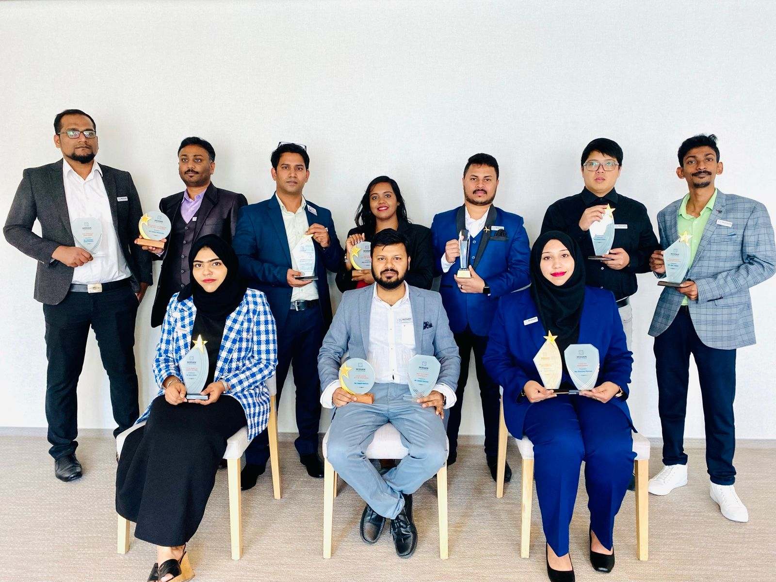 Ten Missan staff in suits holding award trophies, posed against a white wall