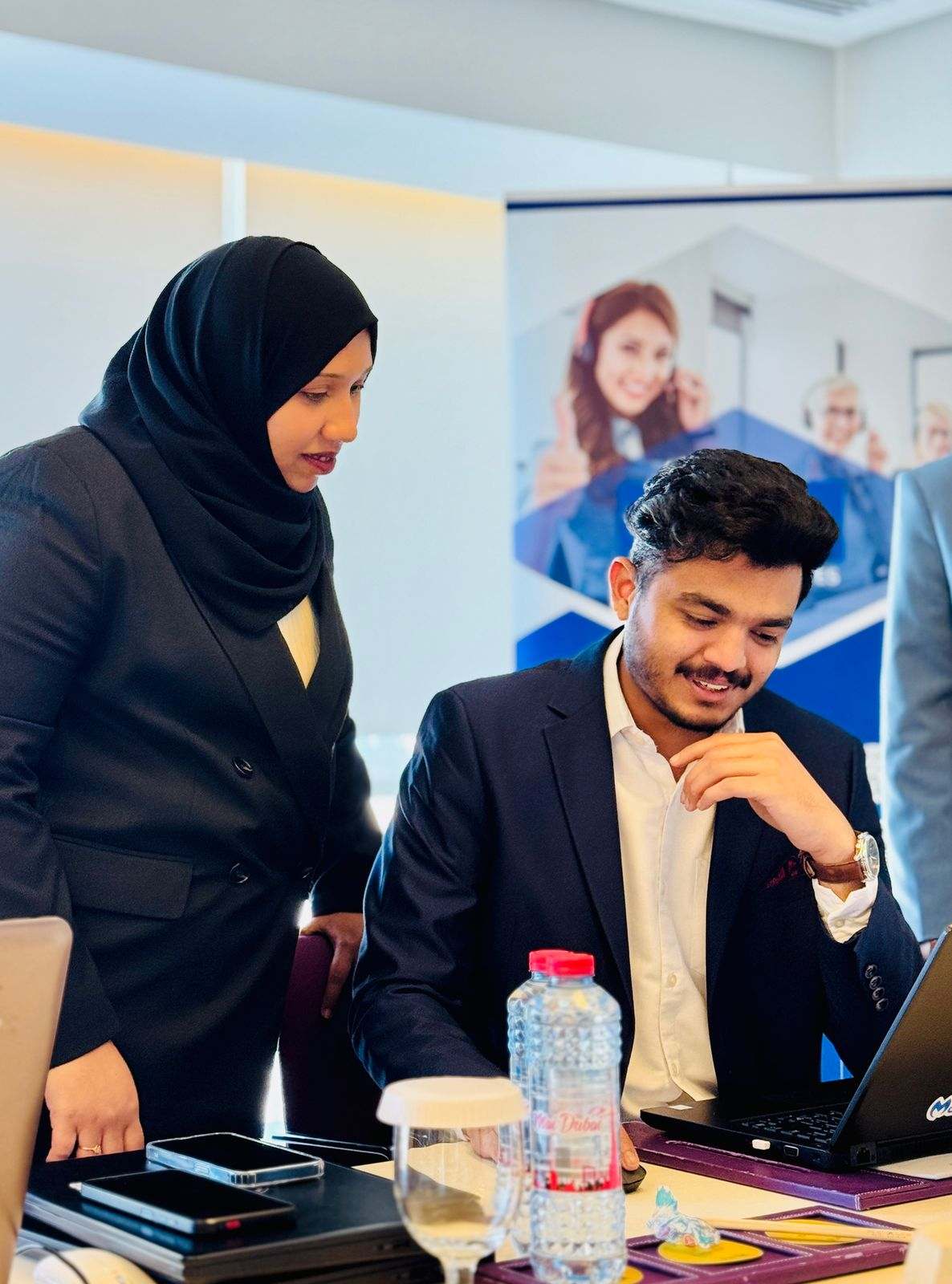 Two Missan colleagues at a laptop, one standing and one seated, with a Missan banner behind