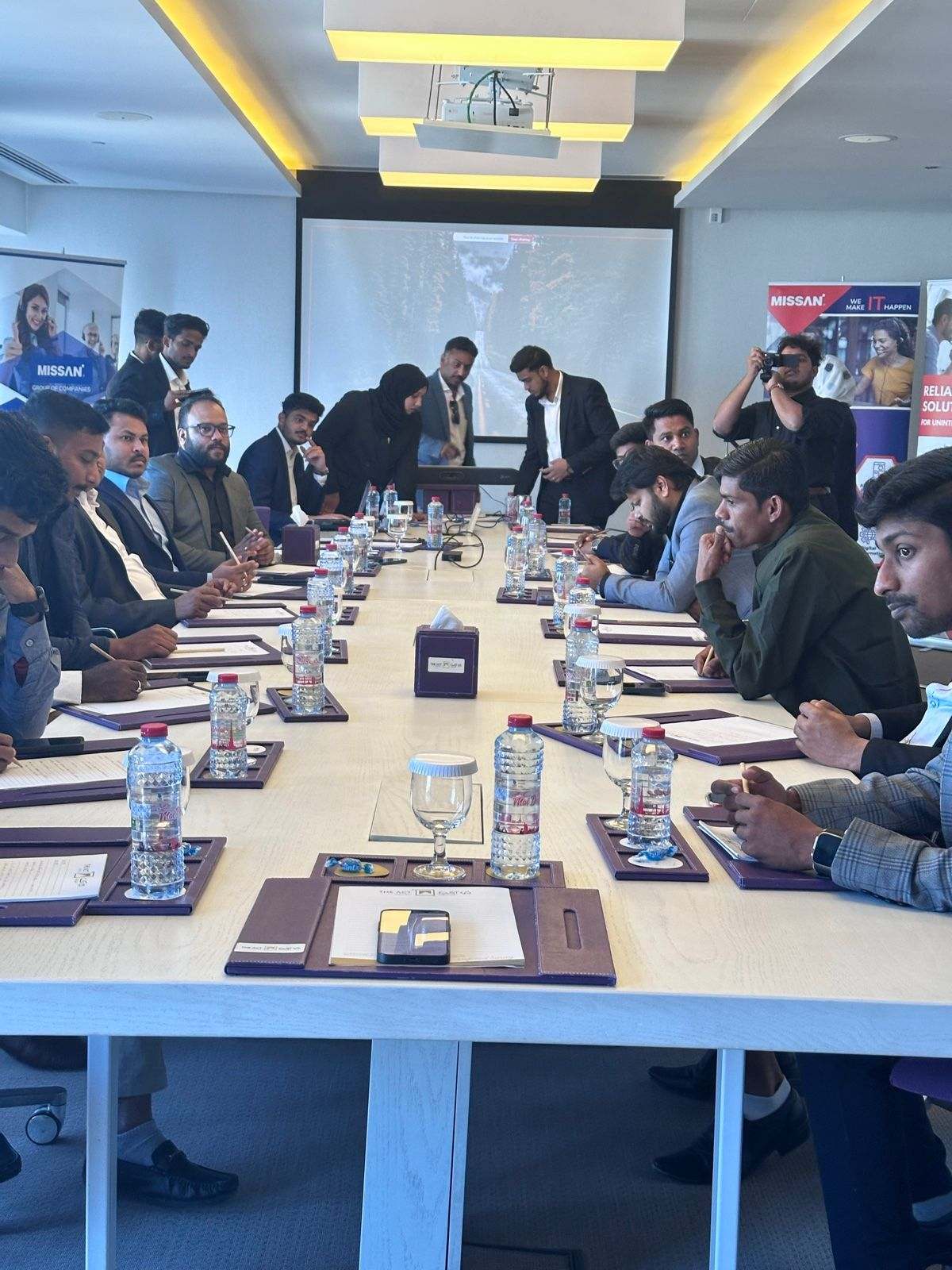 Missan UAE staff seated along both sides of a long boardroom table, with Missan banners at each side of the room