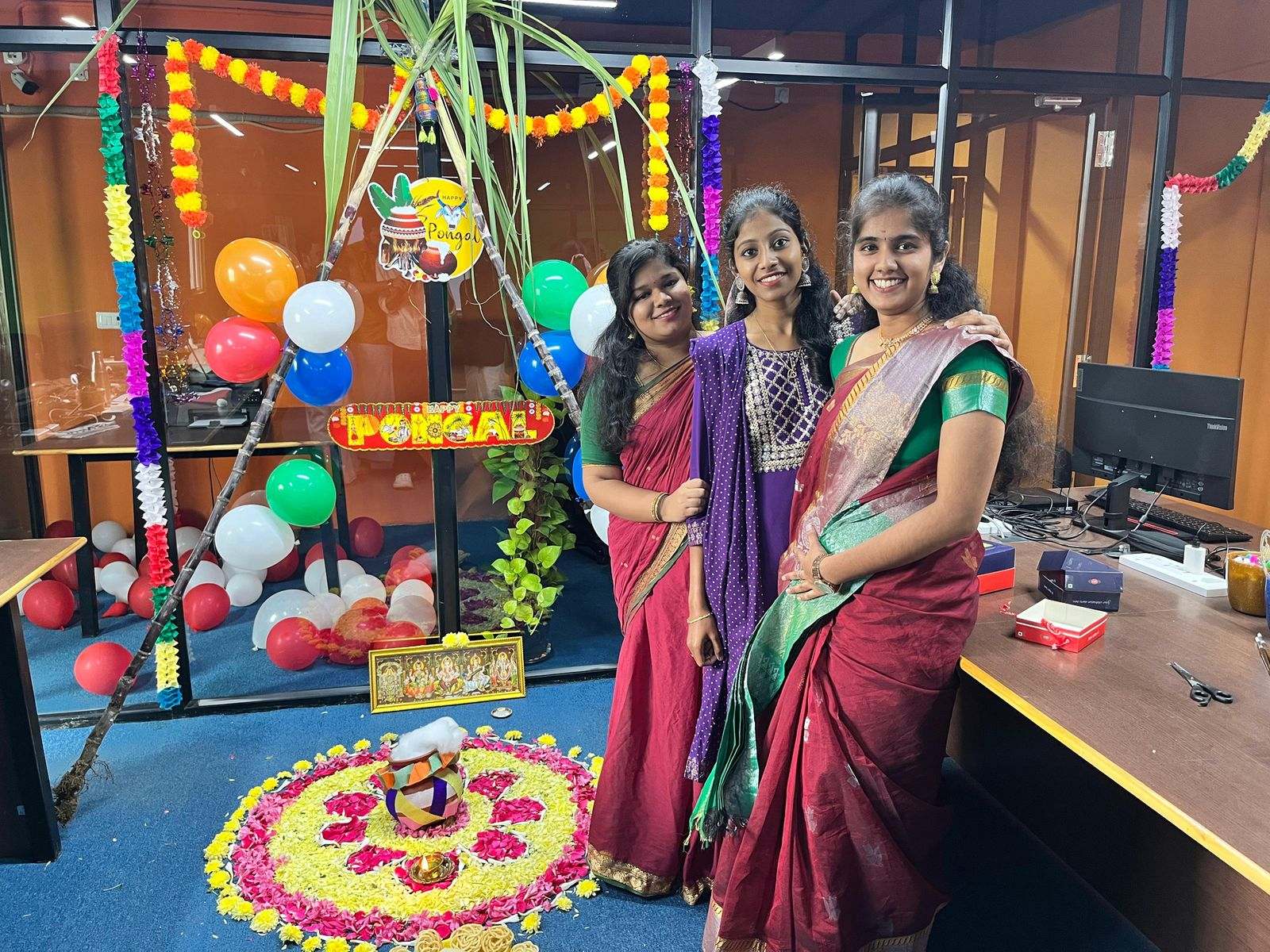 Three women from Missan's India team in sarees beside Pongal decorations and a kolam in their office