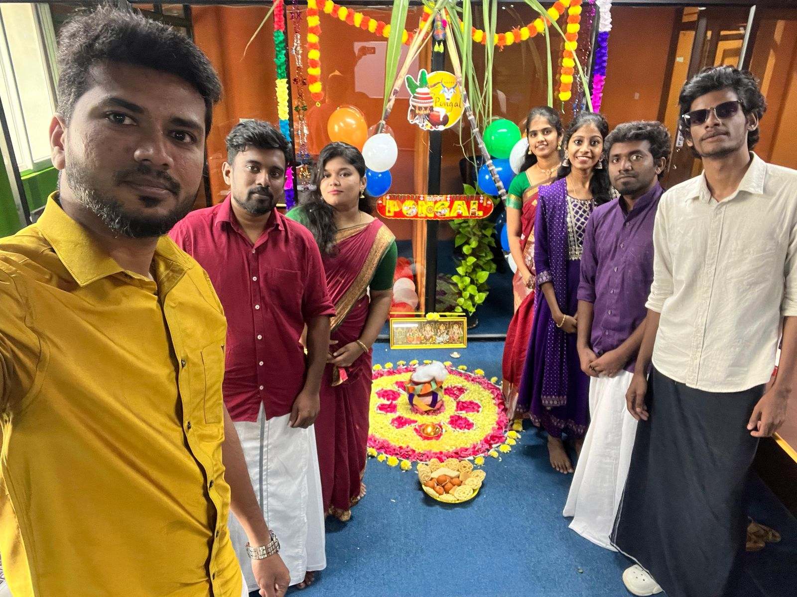Missan's India team of eight at Pongal, in a selfie beside the decorations and a Pongal sign