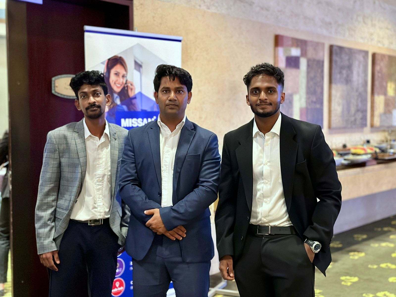 Three men in suits beside a Missan roll-up banner in a hotel function room