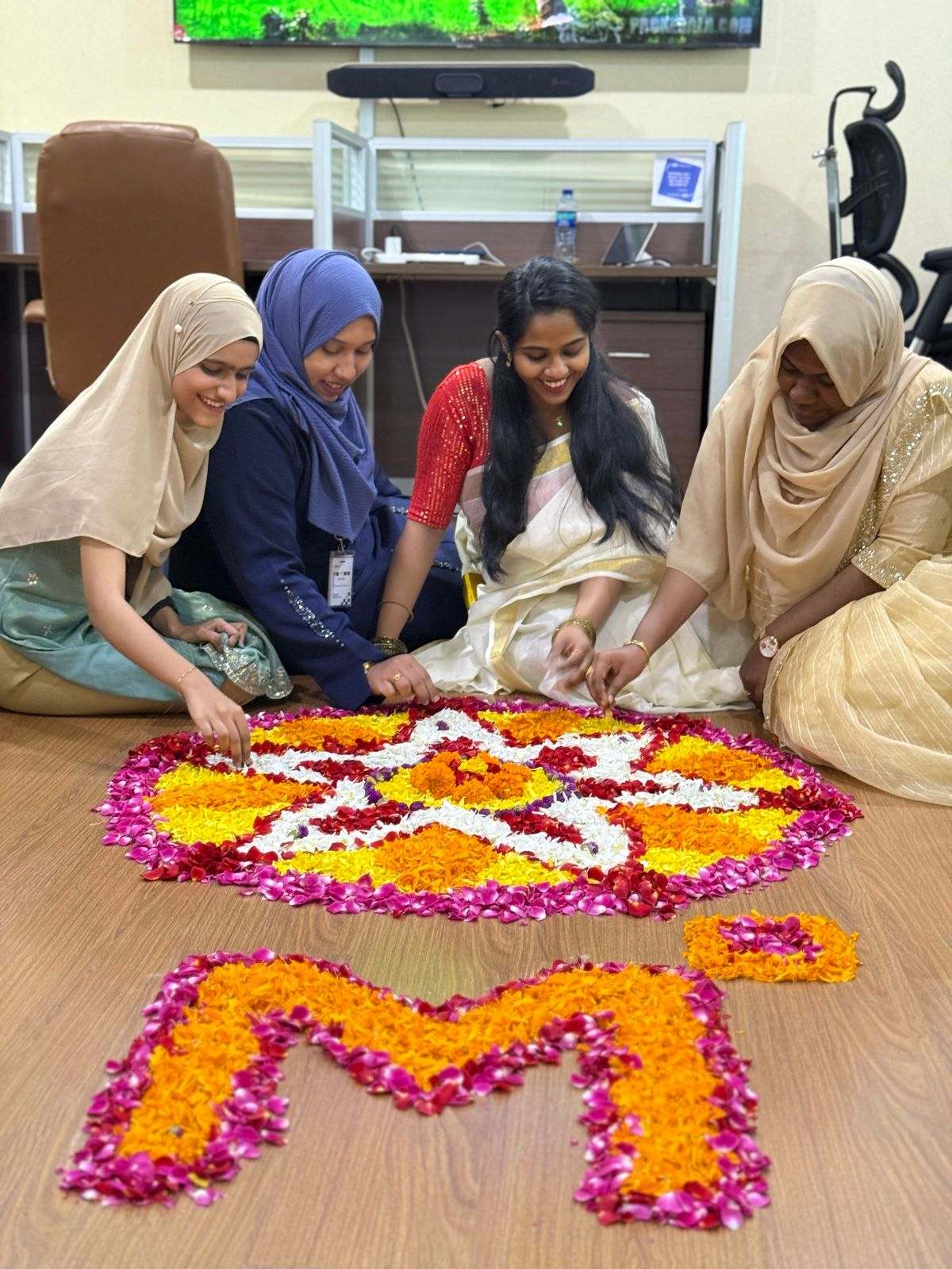 Four Missan colleagues smiling as they lay flower petals for a pookalam shaped like an M